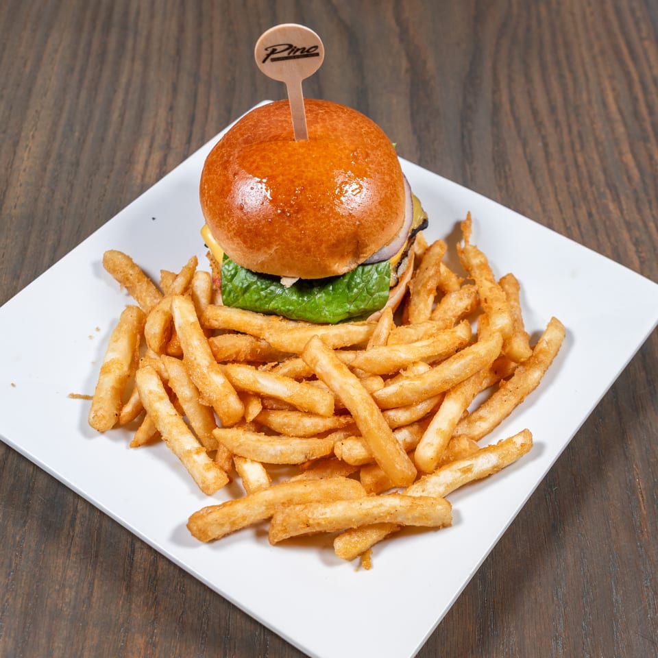 A Pino burger with lettuce, cheese, and onion, served with golden french fries on a white plate.