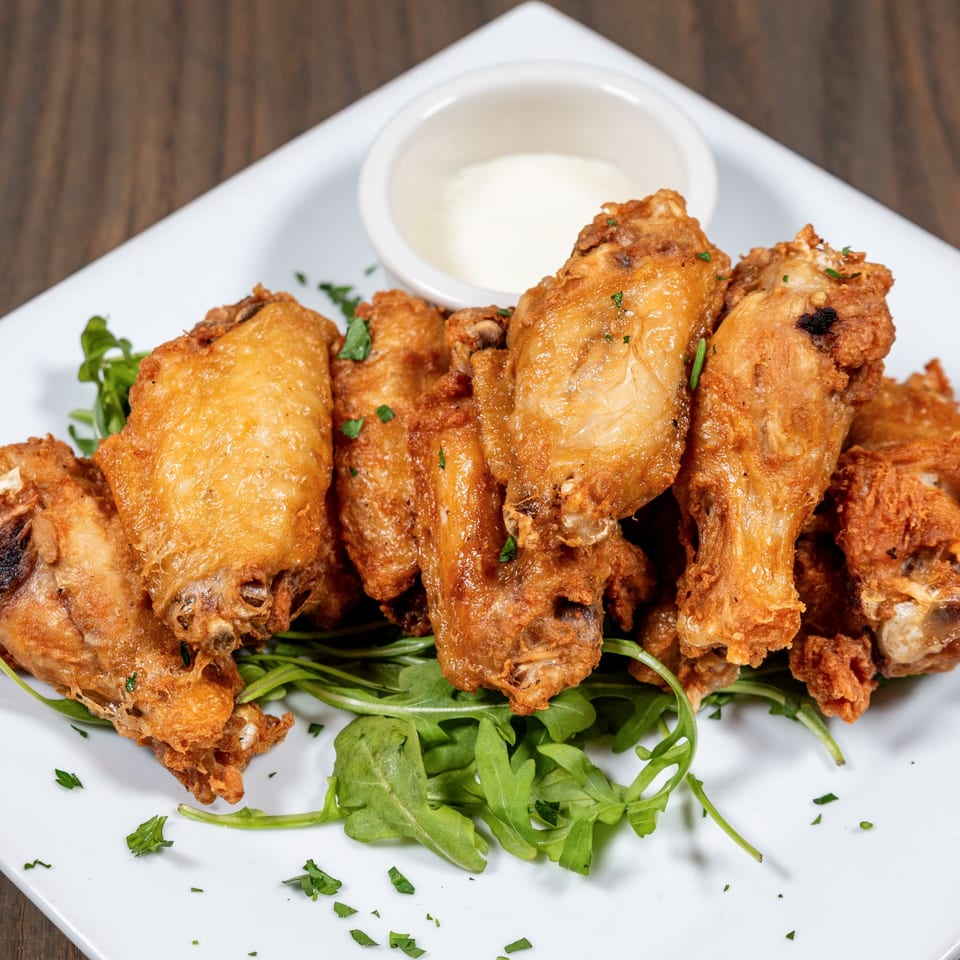 Crispy fried chicken wings on a bed of arugula with a side of white dipping sauce.