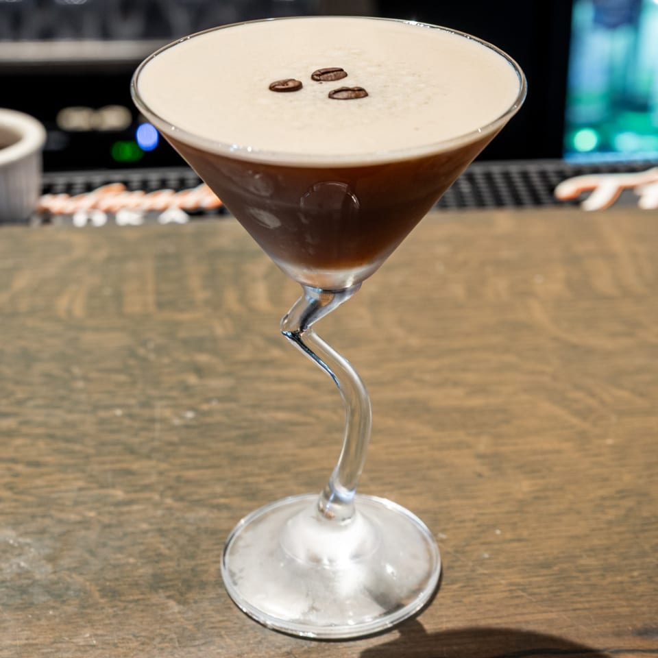 Espresso martini in a unique martini glass with a wavy stem, garnished with three coffee beans.