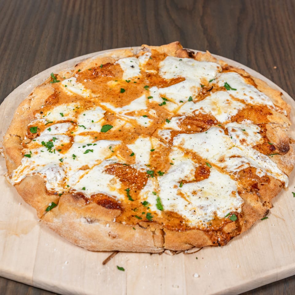 Pino Wine Bar & Bistro's sliced pizza with melted cheese, red sauce, and green herbs on a wooden board.