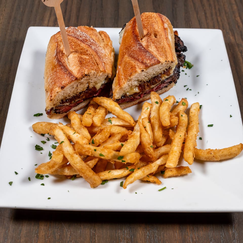A Pino Wine Bar & Bistro steak sandwich with melted cheese and caramelized onions, served with golden fries.